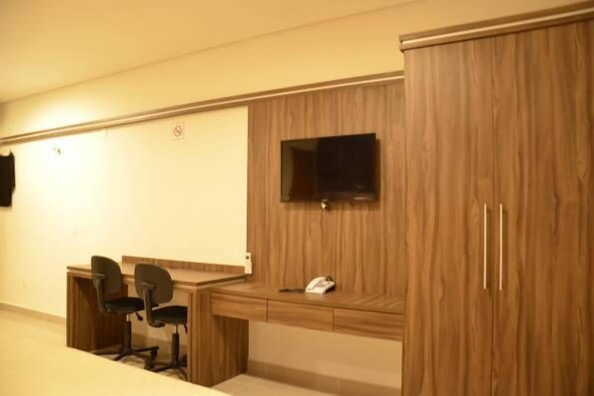 Ein Zimmer mit einem Holztisch, zwei Bürostühlen, einem Telefon und einem an der Wand befestigten Fernseher.