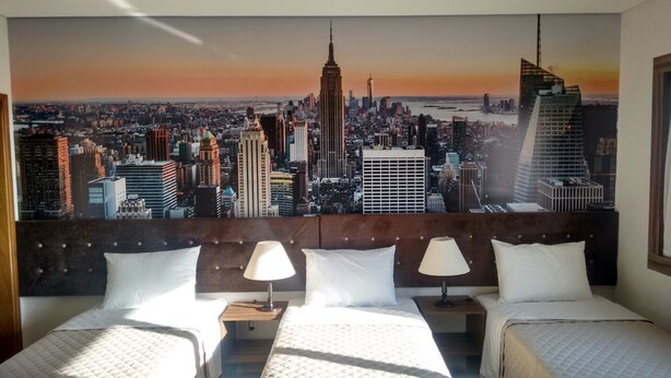Une chambre d’hôtel offrant une vue imprenable sur la ville, dotée d’un lit king-size, de deux tables de chevet avec lampes et d’une tête de lit en bois.