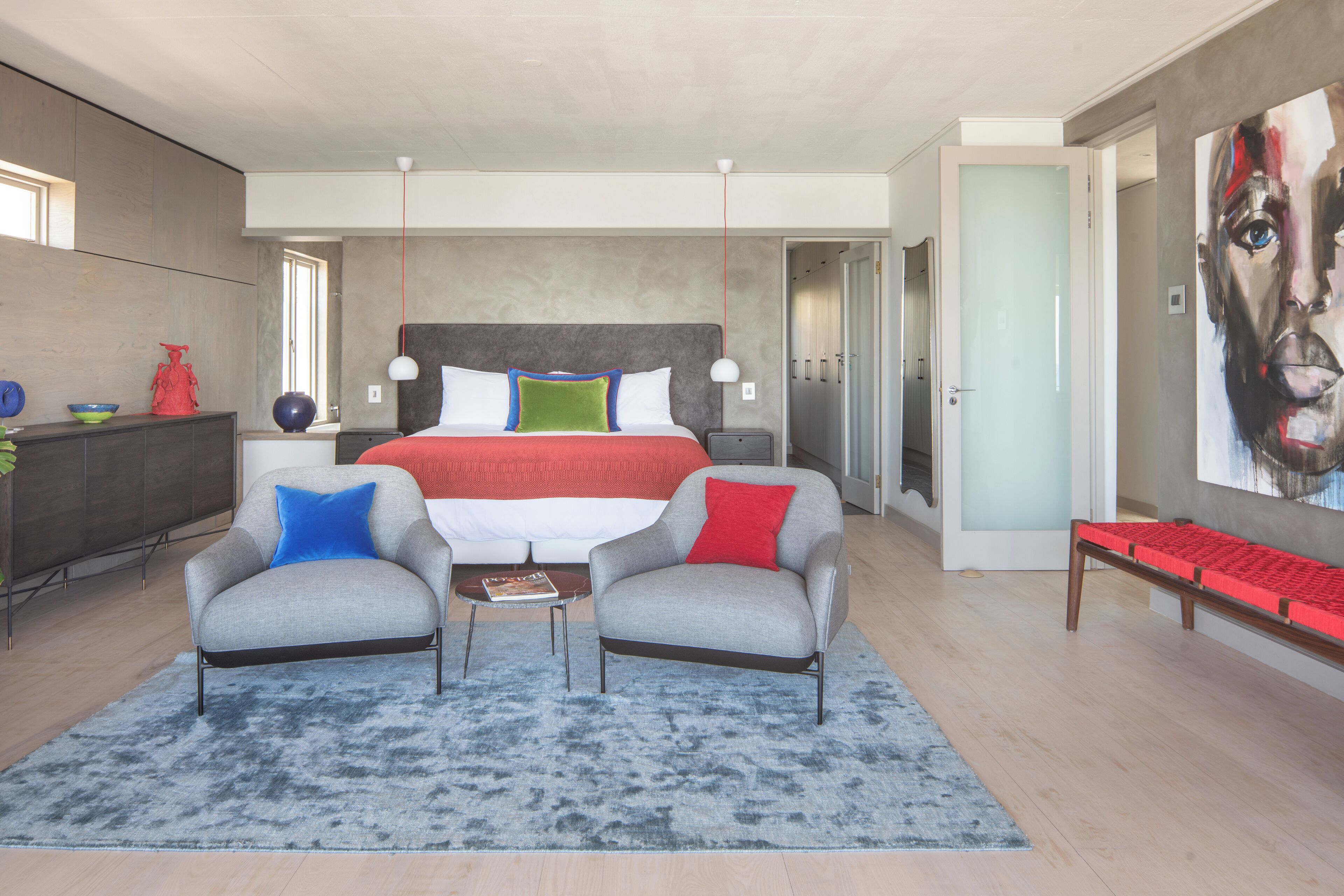 Un dormitorio moderno con una cama grande, dos sillones, una mesita y un banco.