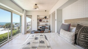 A modern bedroom with a large bed, a view of the sea, and a built-in shelf with decorative items. - 52 Victoria (Cape Town)