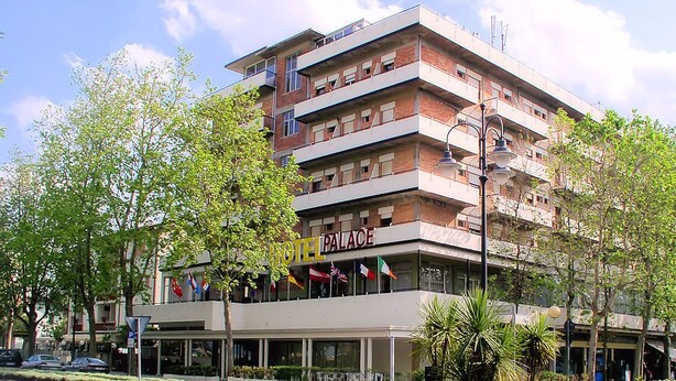 A multi-story hotel with balconies, a sign reading "HOTEL PALACE," and flags. - Hotel Palace (Cesenatico)