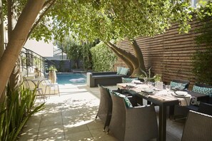 An outdoor patio with a dining table set for two, surrounded by wicker chairs. - Bayflowers Guesthouse (Cape Town)