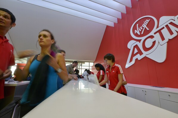 Zona de recepción de Virgin ACTU con una pared roja y un mostrador blanco.