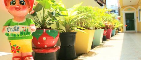 A row of potted plants on a tiled floor, with a decorative figure in the foreground.