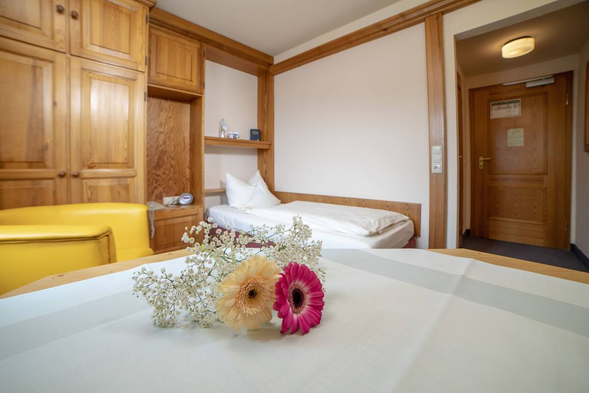 A hotel room with wooden cabinets, a bed, a bedside table with a lamp, and a small shelf with toiletries.