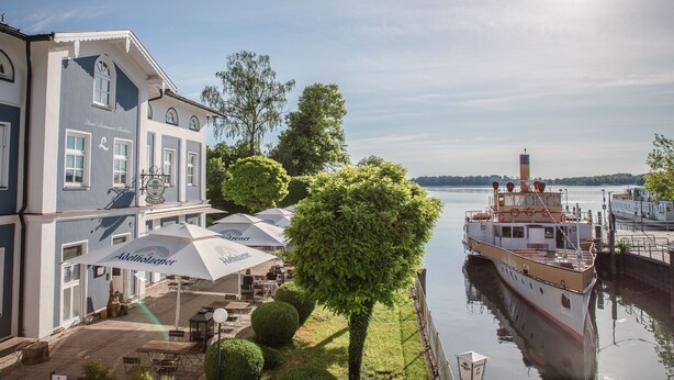 Ein Hotel am Flussufer mit Außenbestuhlung und einem angemeldeten Boot in der Nähe.
