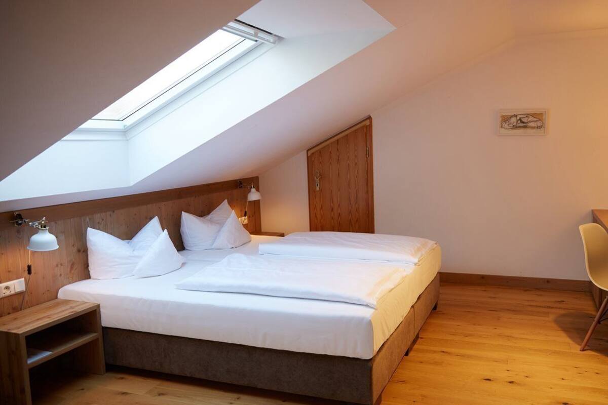 A bedroom with a skylight, a bed, a desk, and a chair.