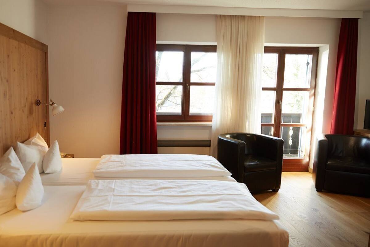 A hotel room with a large bed, two bedside tables, a chair, and a window with curtains.