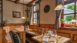 Ein gemütlicher Essbereich mit Holzbänken und -tischen, einem Kruzifix an der Wand und einem Fenster mit Vorhängen.