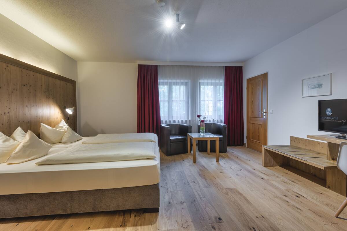 A hotel room with a bed, a desk, a chair, a TV, and a window with curtains.