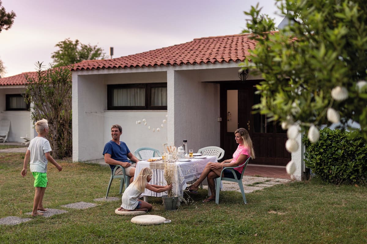 A patio with a table set for a meal, surrounded by a house with a tiled roof and a small garden.