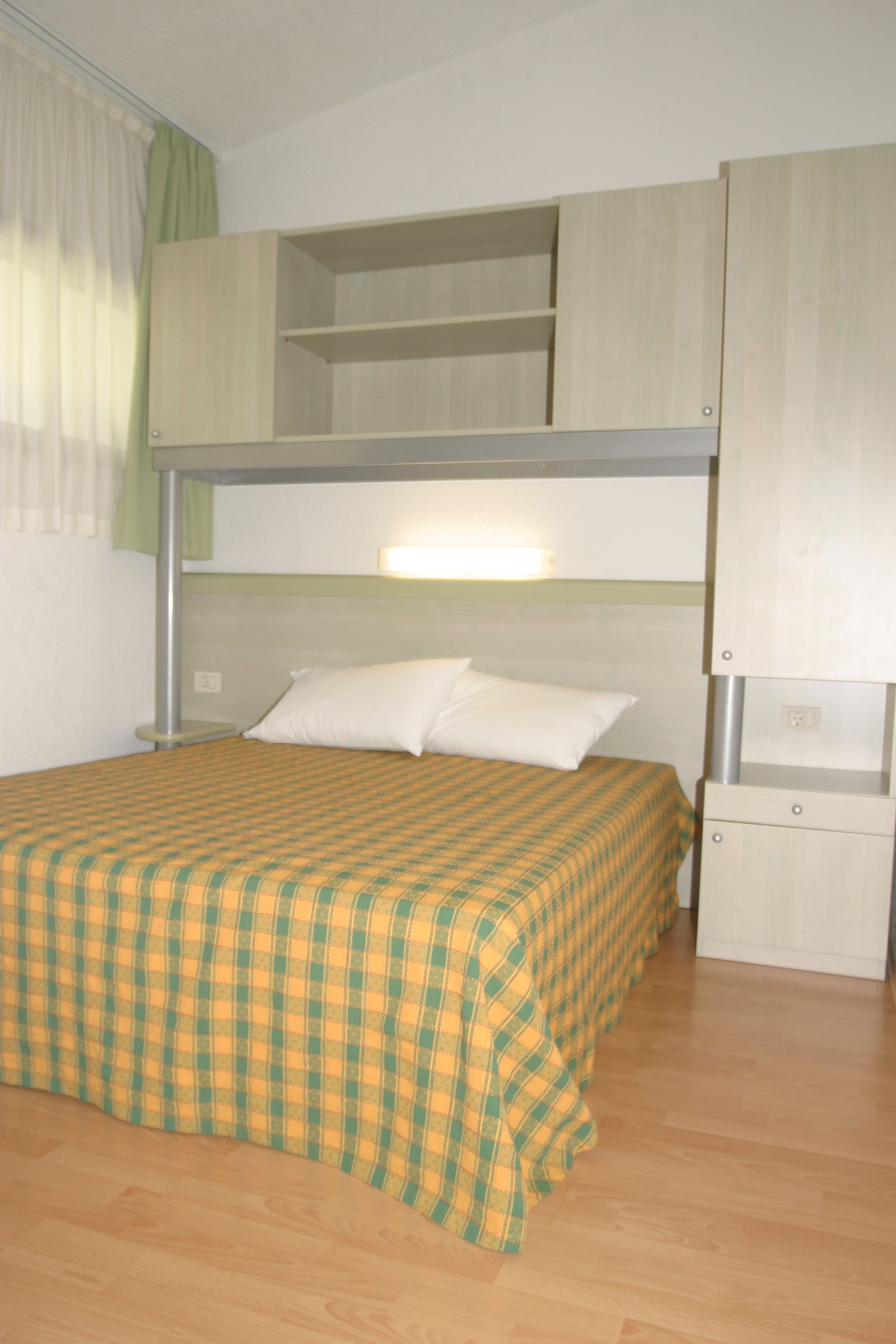 A bunk bed with a checkered bedspread, a bedside table, and a wardrobe with multiple compartments.