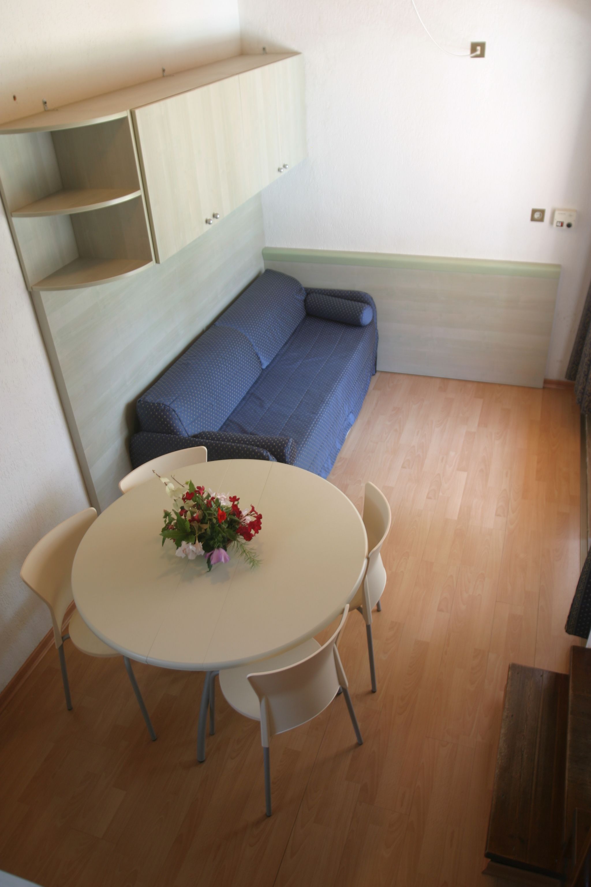 A compact living space with a round dining table, a sofa, and built-in wooden shelving.
