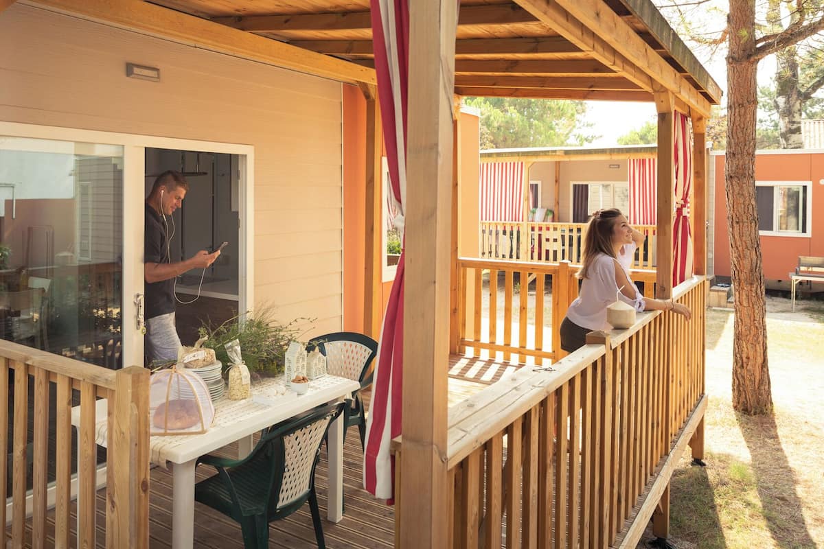 A wooden deck with a table and chairs, a glass door, and a small garden area with plants.