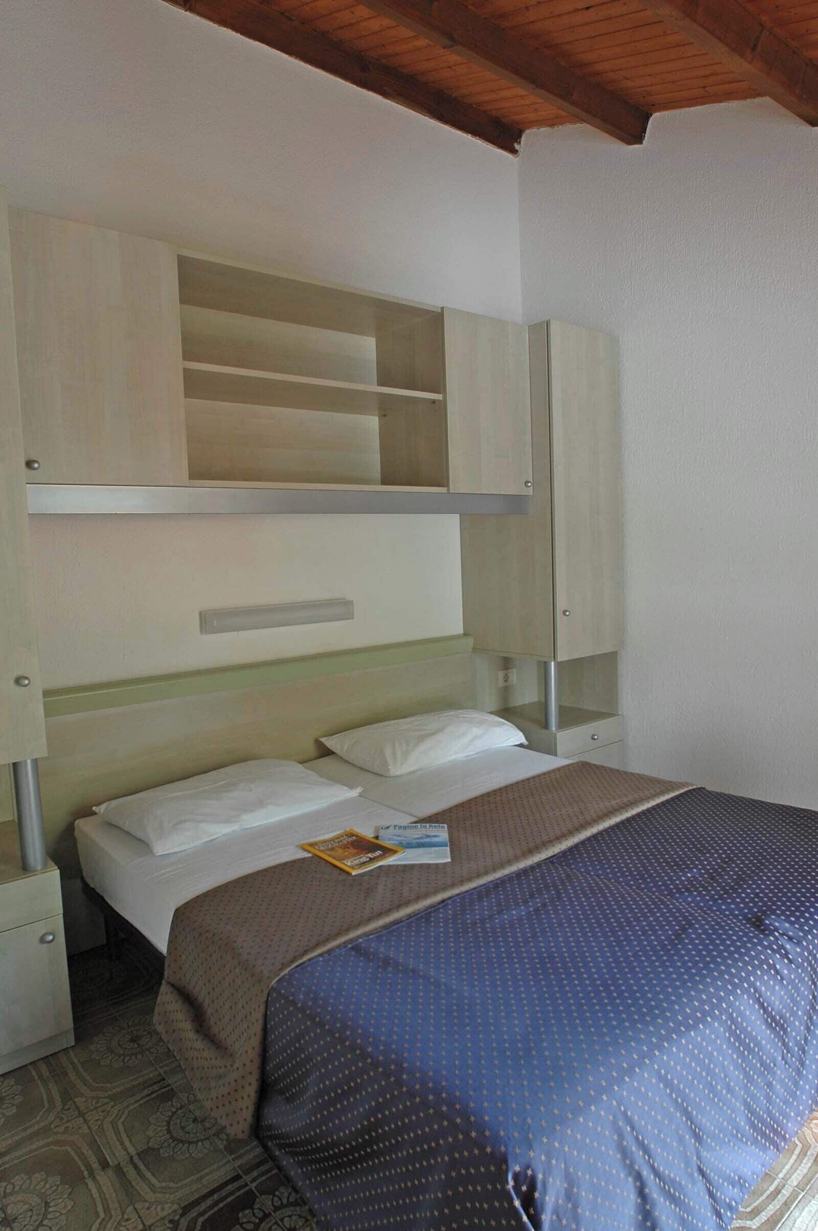 A hotel room with a bunk bed, a small bedside table, and a built-in shelf above the bed.