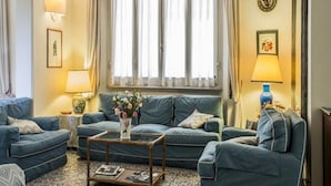 Ein gemütliches Wohnzimmer mit blauem Sofagarnitur, einem Couchtisch und einem Fenster mit Vorhängen.