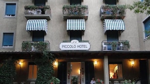 Das Außengelände des Piccolo Hotels mit einem Schild, Sitzgelegenheiten im Freien und Pflanzkübeln.