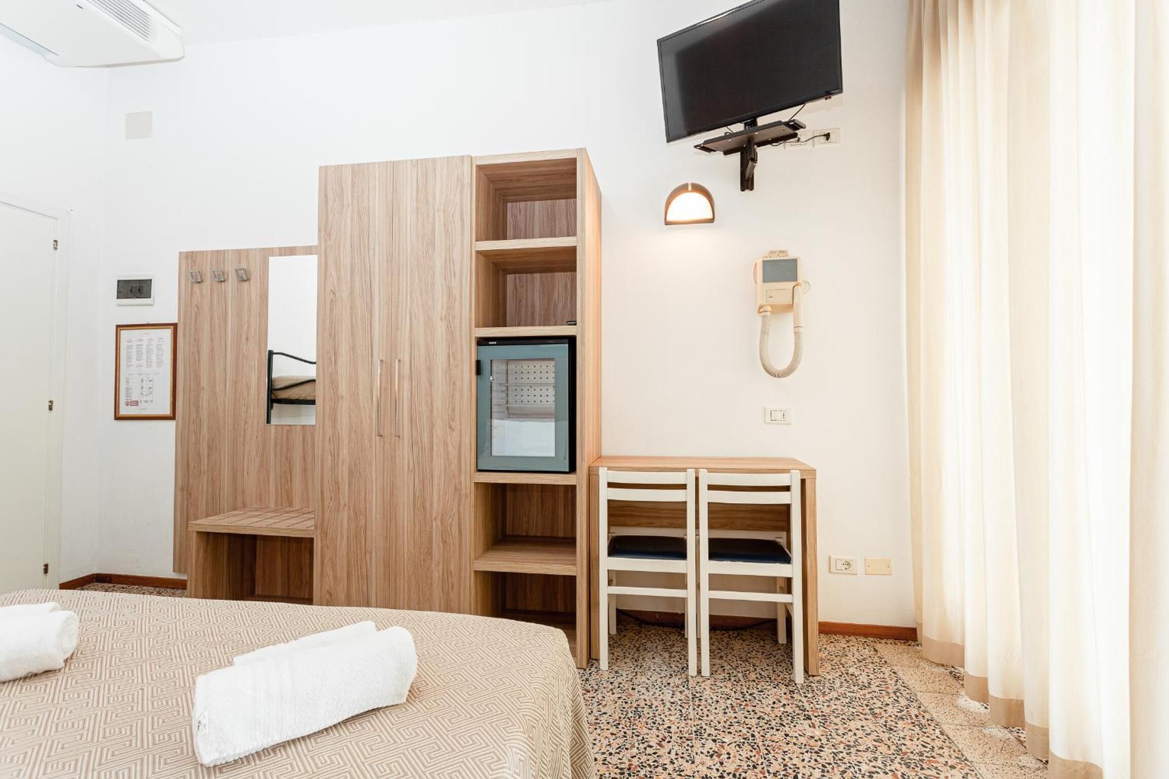 A hotel room with a bed, a wooden wardrobe, a television, a desk, and a phone.