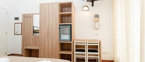 A hotel room with a bed, a wooden wardrobe, a television, a desk, and a phone.