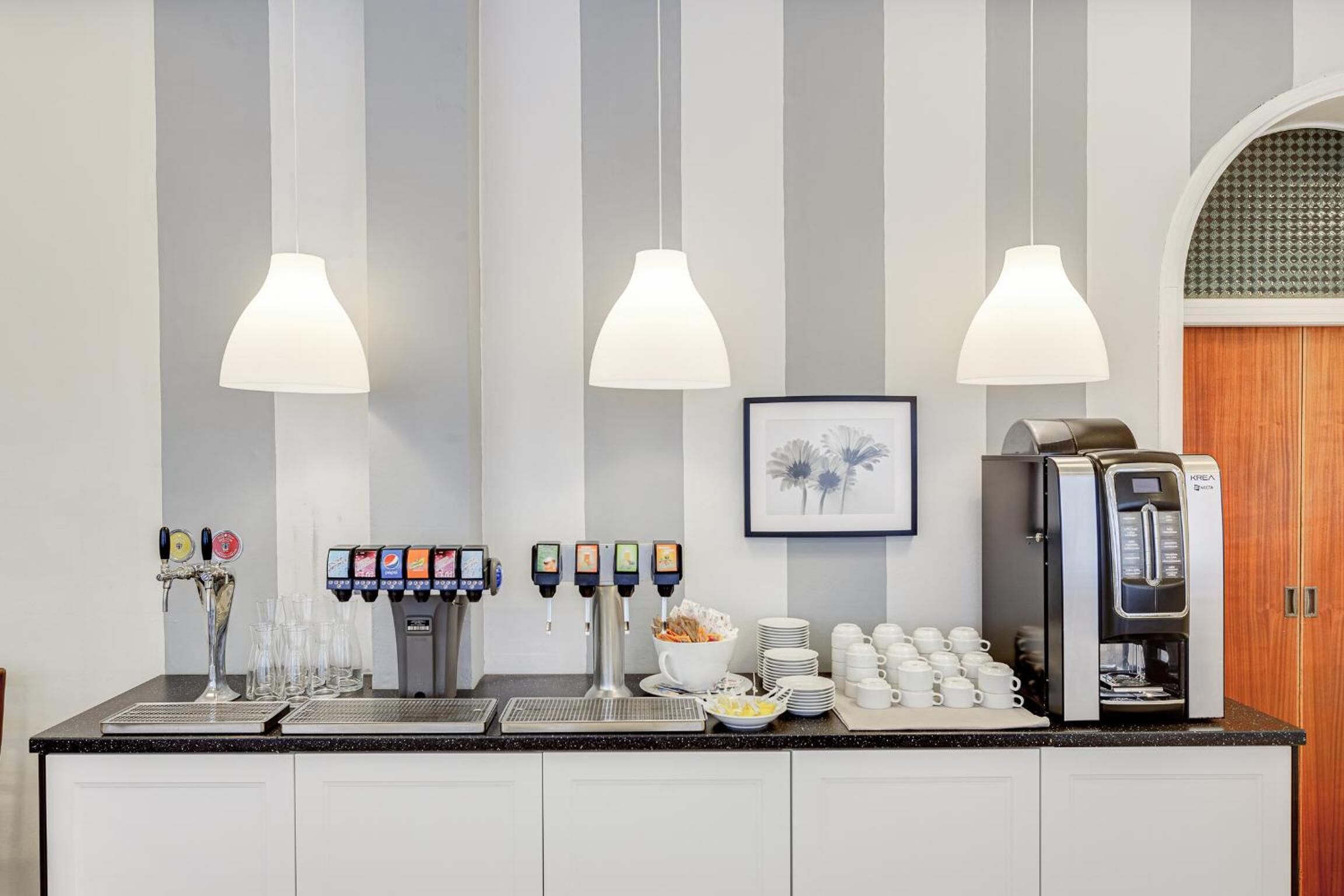 A self-service coffee station with multiple beverage dispensers, a coffee machine, and a variety of cups and mugs.