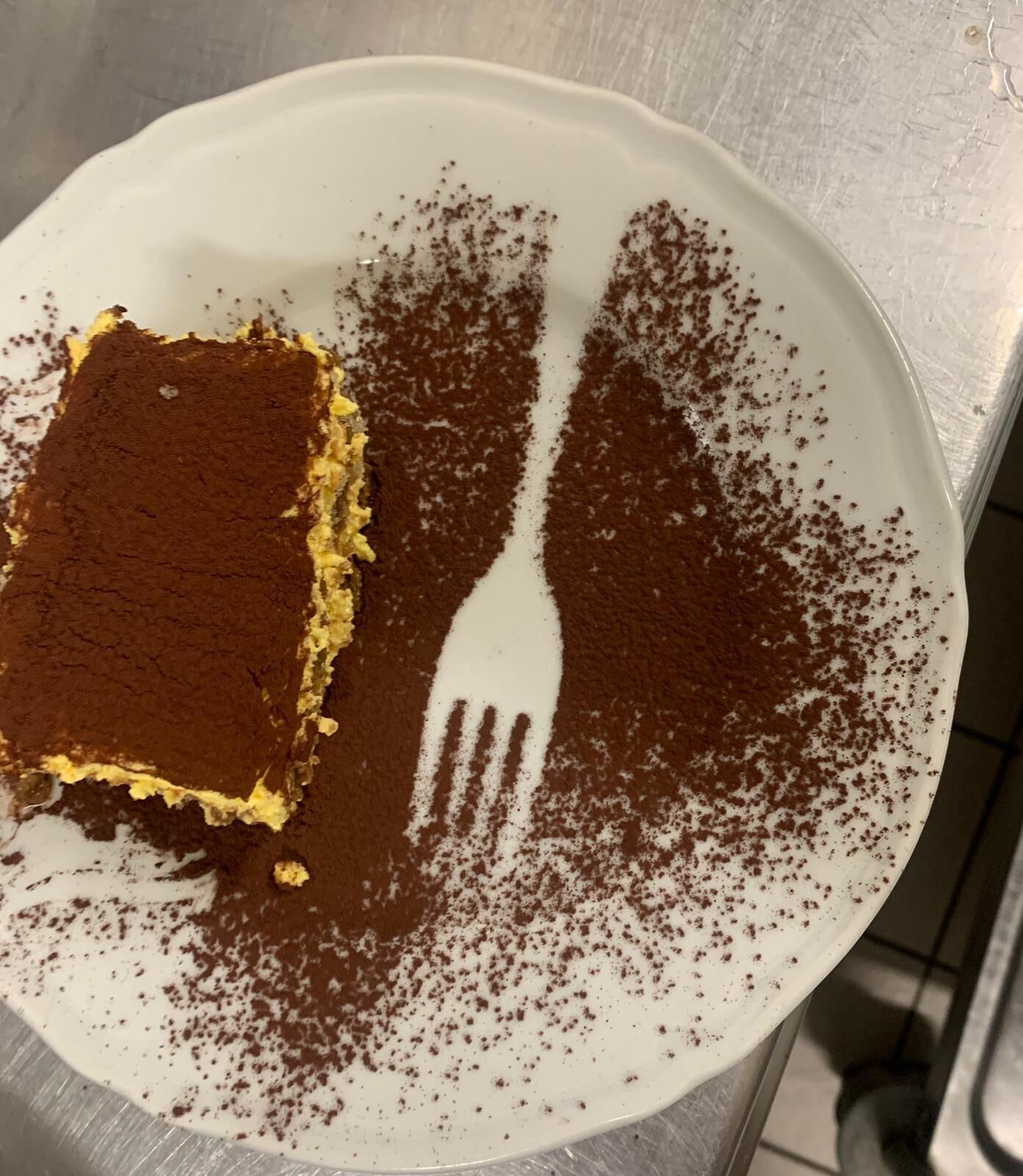 A white plate with a piece of tiramisu and a fork.