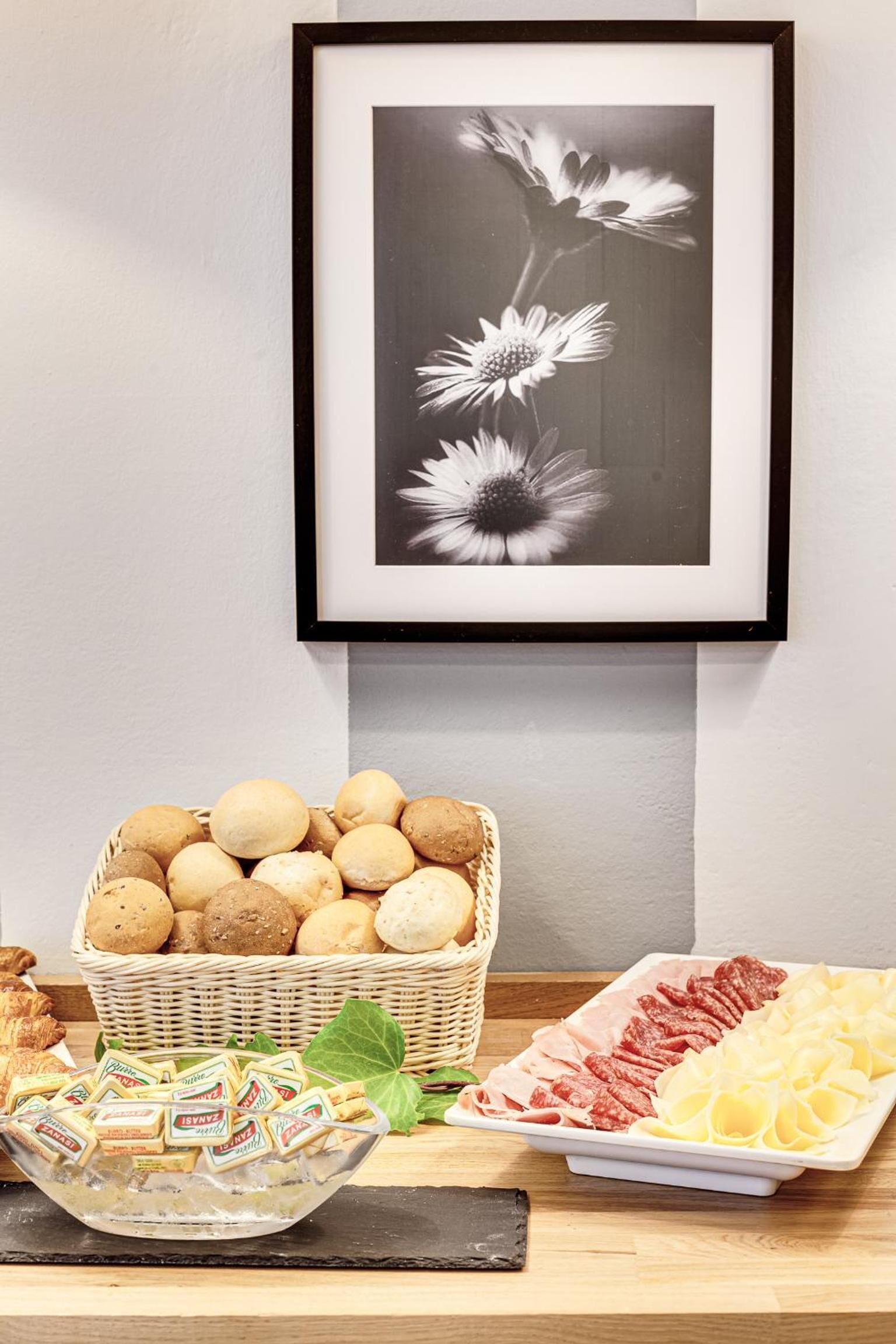 A buffet table with a basket of bread rolls, a bowl of cheese cubes, and a plate of sliced meats.