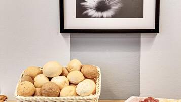 A buffet table with a basket of bread rolls, a bowl of cheese cubes, and a plate of sliced meats.