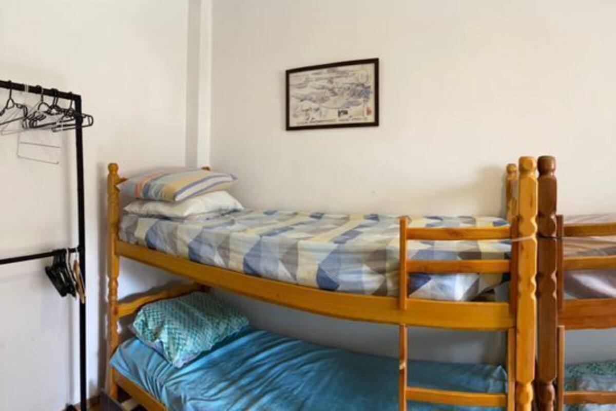Une chambre de dortoir avec des lits superposés, un ventilateur, une fenêtre avec des rideaux et un petit bureau avec un ordinateur.