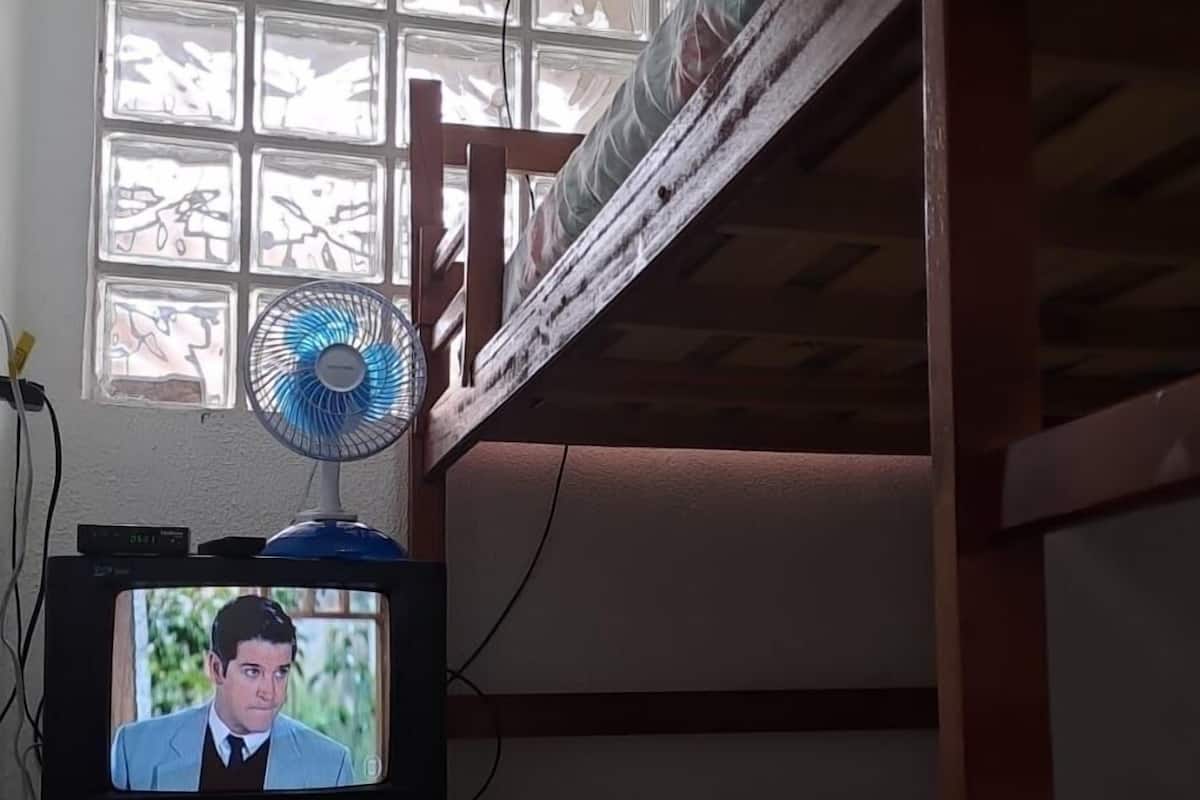 Une chambre avec un lit superposé, un téléviseur posé sur un meuble et une fenêtre donnant sur un paysage verdoyant.