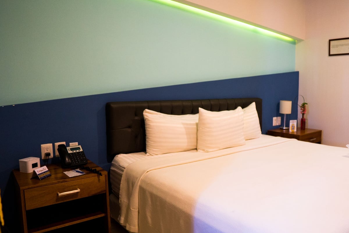 A hotel room with a bed, a nightstand, a phone, and a lamp.