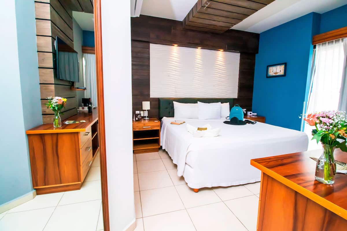 A hotel room with a large bed, a wooden desk, a TV mounted on the wall, and a window with curtains.