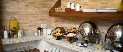 A breakfast buffet setup with various food items, glassware, and serving utensils.