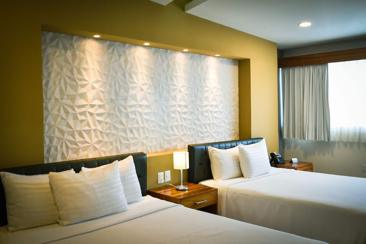 A hotel room with two beds, a geometric-patterned wall, a wooden nightstand, and a window with curtains.
