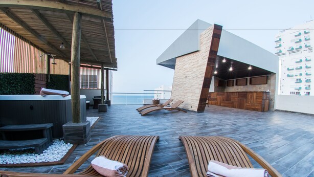Un espace de détente sur le toit, avec des chaises longues en bois, un jacuzzi et une vue sur la mer.