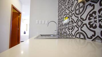 A kitchen with a white countertop, a stainless steel sink, and a patterned backsplash.