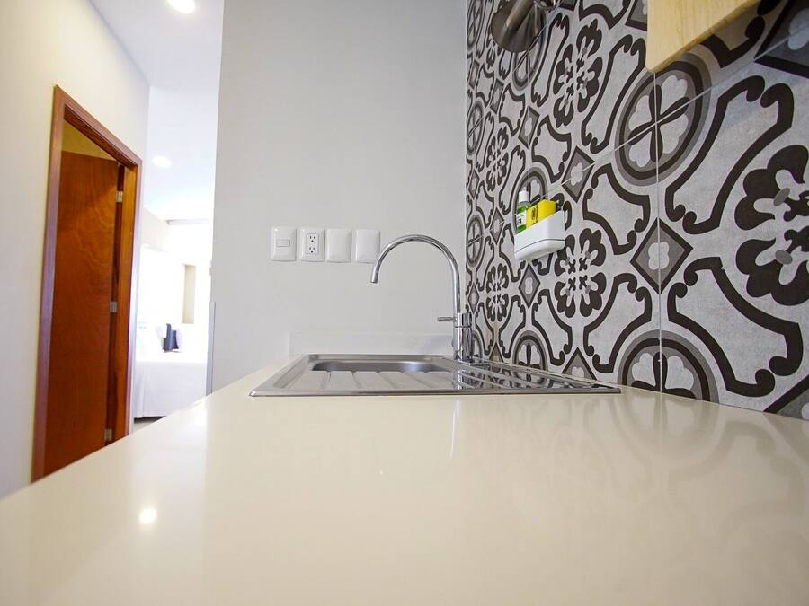 A kitchen with a white countertop, a stainless steel sink, and a patterned backsplash.
