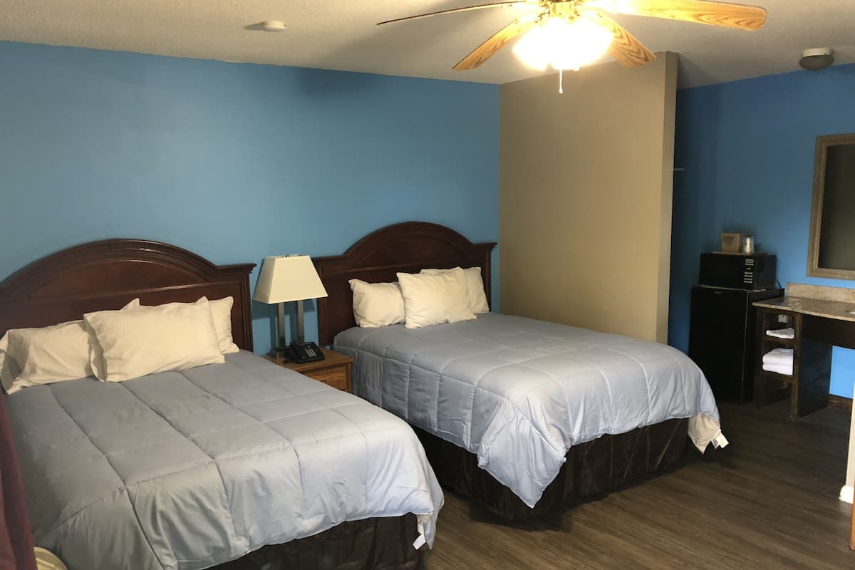 Une chambre d’hôtel avec deux lits, un ventilateur de plafond, un bureau avec un ordinateur et un four à micro-ondes.
