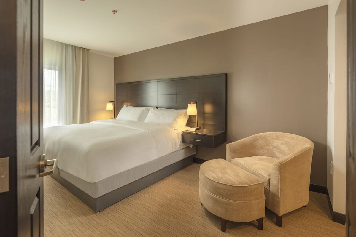A hotel room with a large bed, bedside lamps, a chair, and a nightstand.
