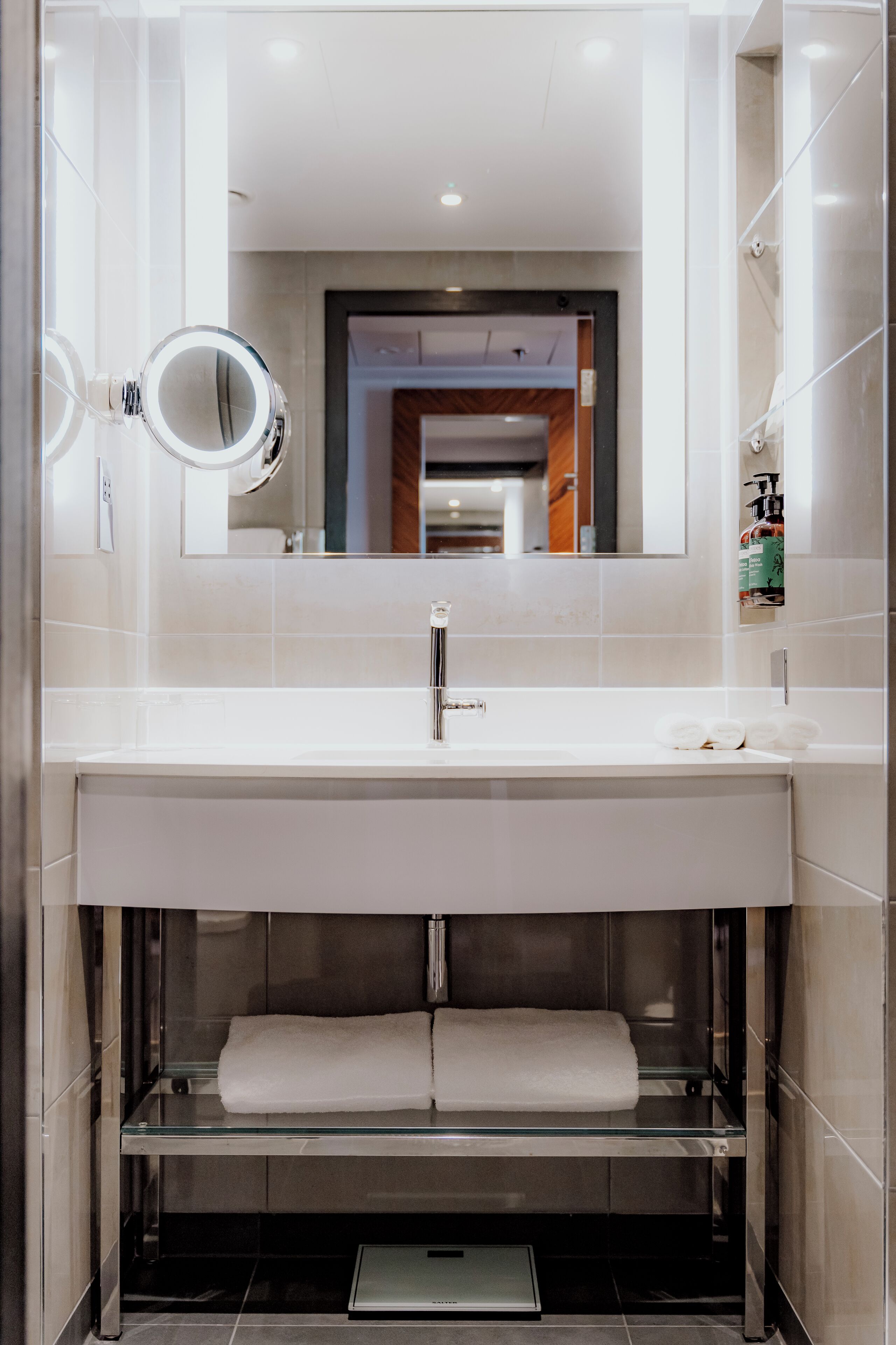 Un baño moderno con un espejo grande, un lavabo blanco y una ducha con mampara de vidrio.