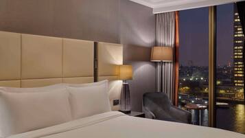 Una habitación de hotel con una cama grande, una mesita de noche, una lámpara, una silla y vistas a un paisaje urbano nocturno.