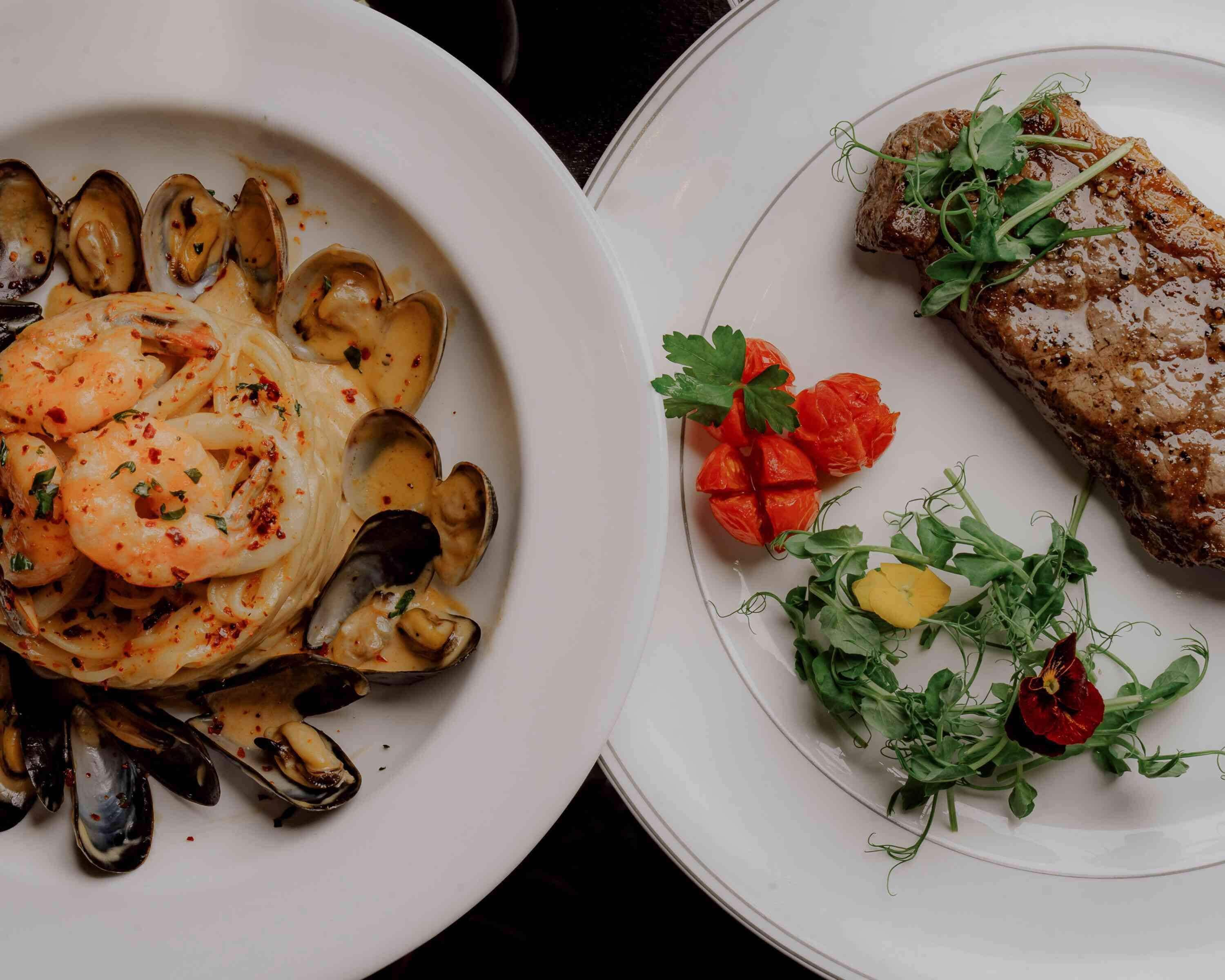 Two plates of food, one with mussels and shrimp, and the other with a steak and greens.