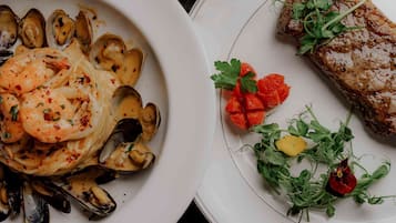 Two plates of food, one with mussels and shrimp, and the other with a steak and greens.