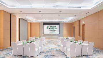 A conference room with a large screen displaying 'Holiday Inn' branding, white chairs, and tables set for a meeting.