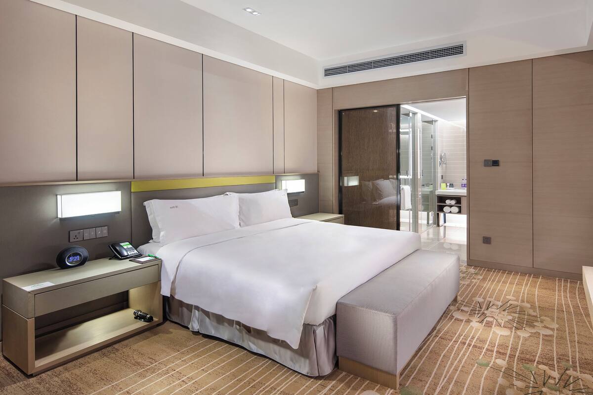 A modern hotel room with a bed, bedside table, lamp, and a TV.