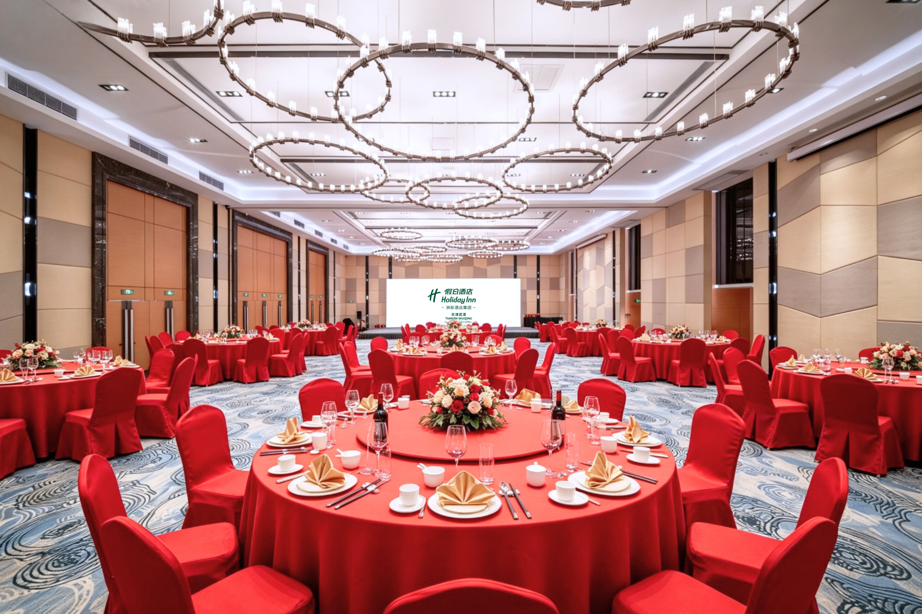 Un salón de conferencias con mesas redondas, sillas rojas y una pantalla grande al frente.