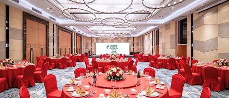 Un salón de conferencias con mesas redondas, sillas rojas y una pantalla grande al frente.