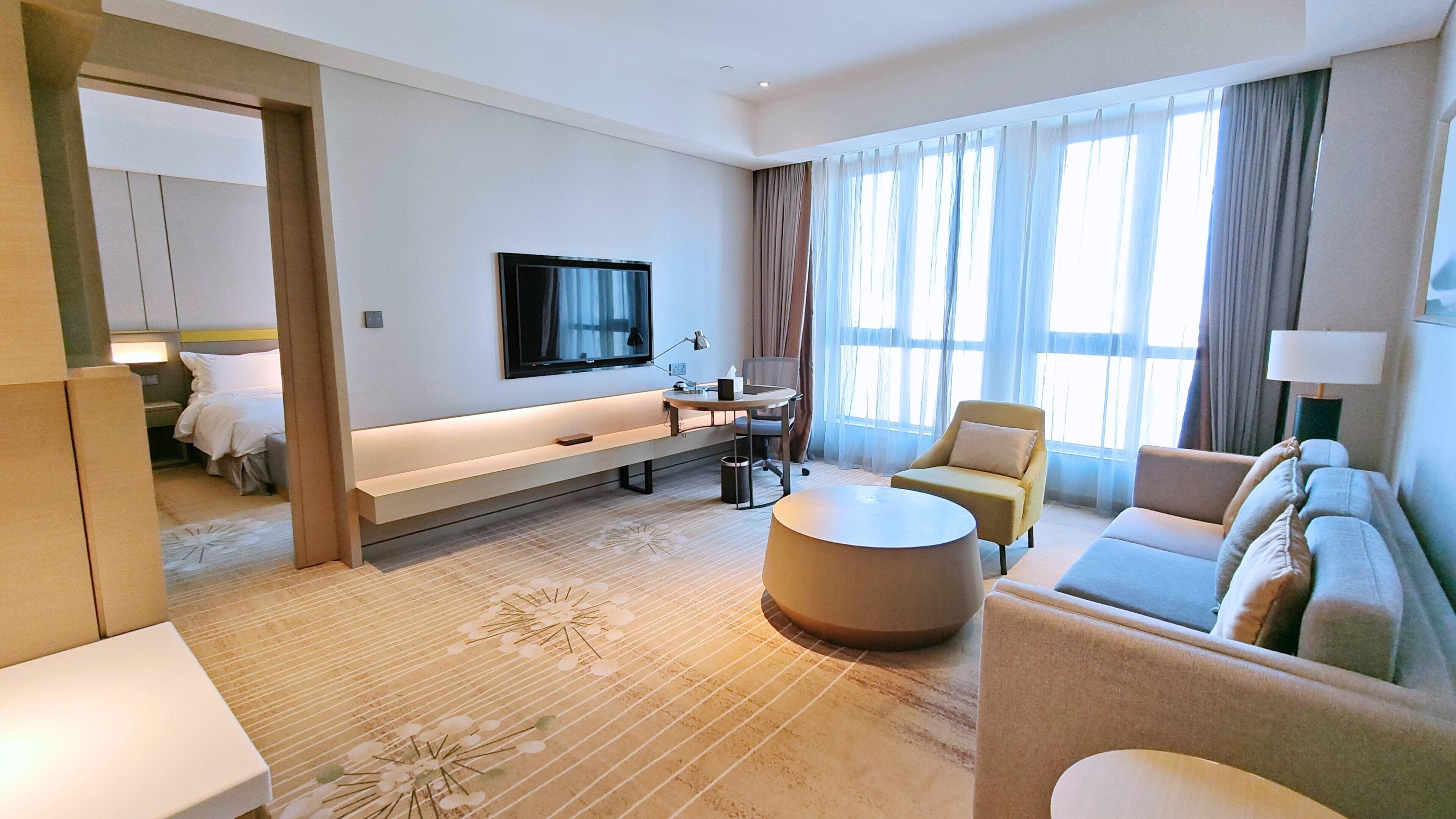 Habitación de hotel con cama, sofá, mesa de centro, televisor y escritorio con silla.