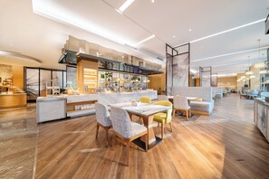 En modern restaurang med en bänkskiva i marmor, trästolar och ett högt tak med linjeformad belysning.