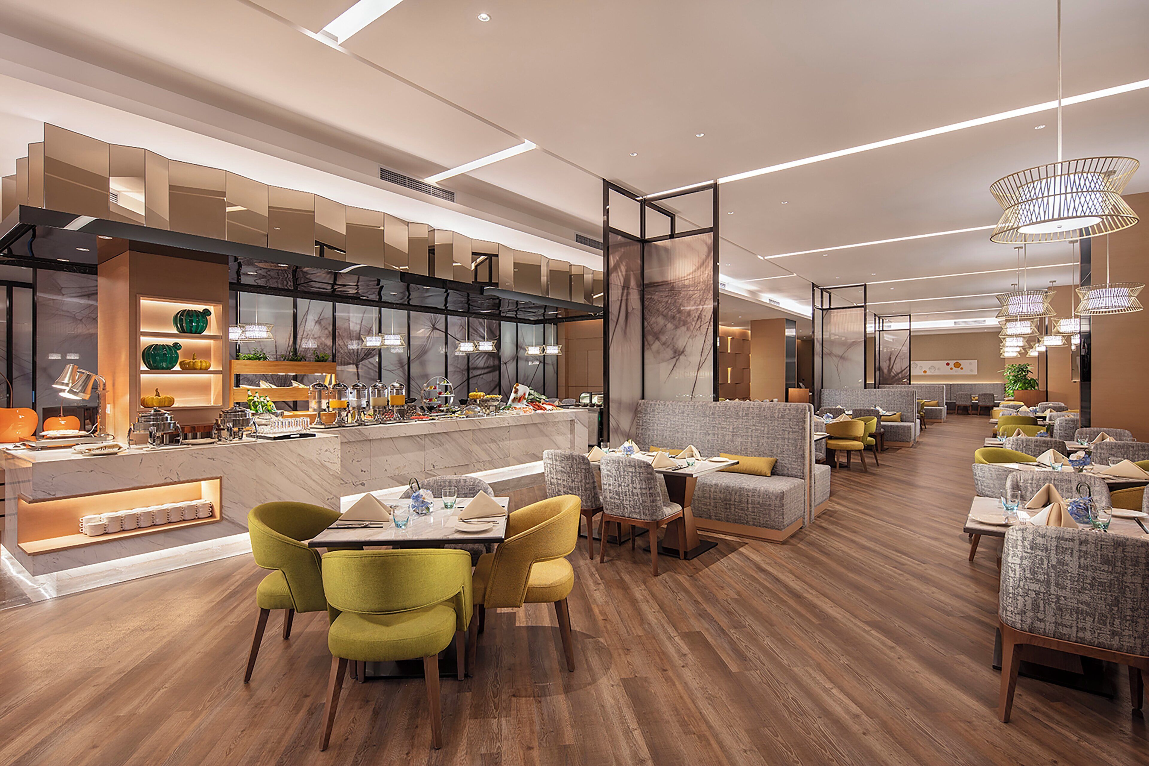 Ein modernes Restaurant mit Holzboden, grünen und gelben Stühlen und einer Bar mit einer Marmorplatte.