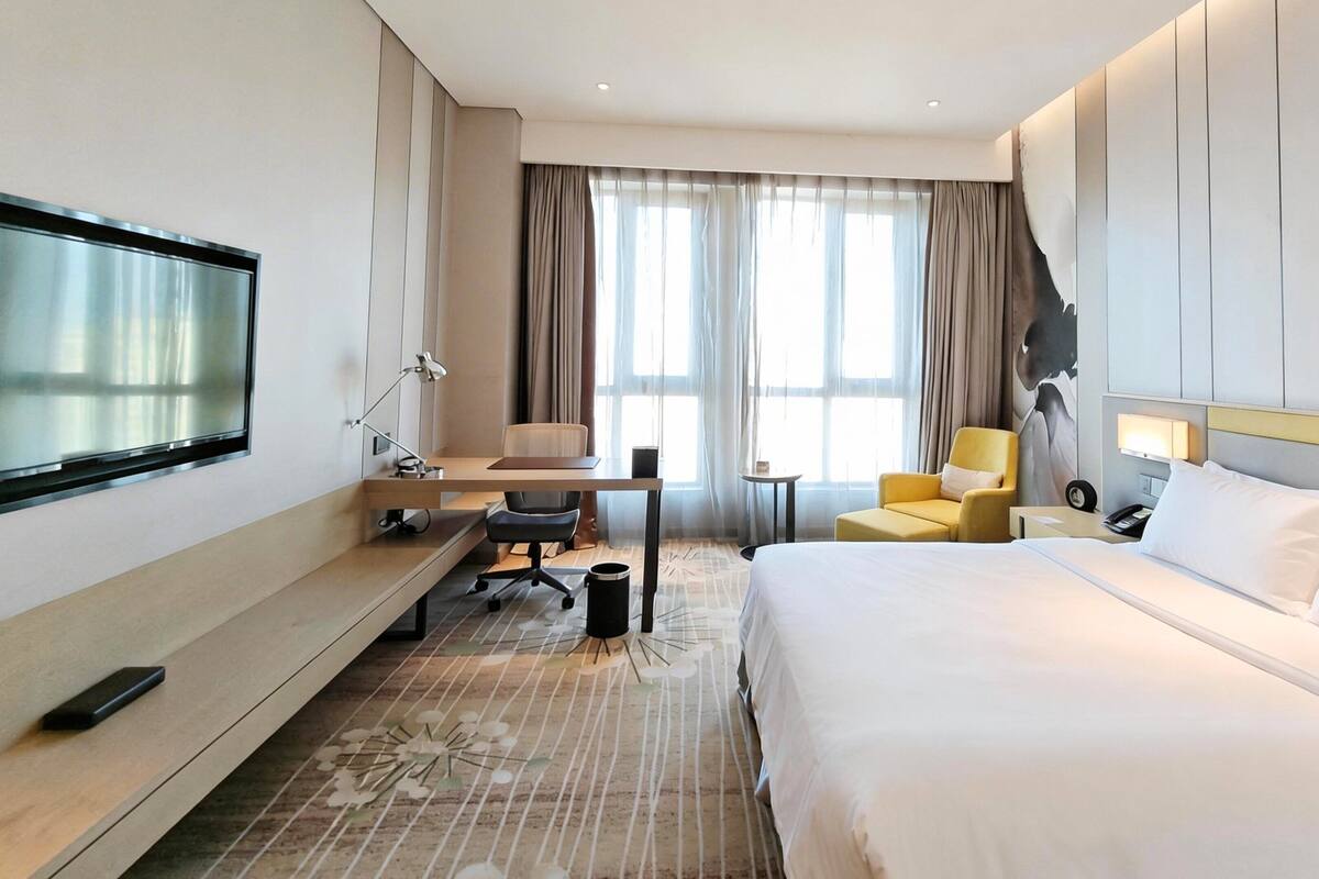 A hotel room with a bed, a desk, a chair, a TV, and a window with curtains.